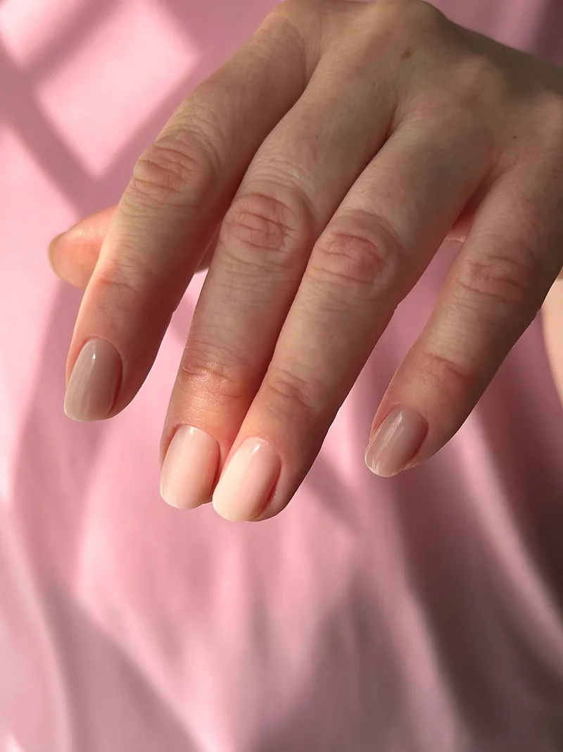 Short oval nails in soft nude gel on a pink background